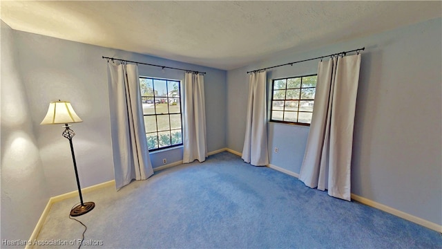 spare room featuring light carpet, a textured ceiling, and baseboards