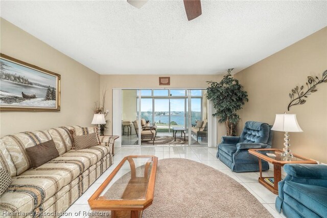 living room featuring ceiling fan, light tile patterned floors, a water view, and a textured ceiling