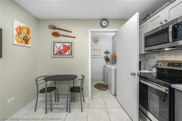 kitchen with washing machine and clothes dryer, stainless steel appliances, white cabinets, backsplash, and light tile patterned flooring