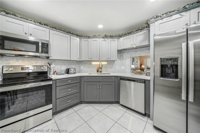 kitchen featuring gray cabinetry, sink, decorative backsplash, light tile patterned flooring, and appliances with stainless steel finishes