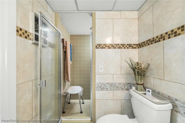 bathroom with a shower with door, toilet, and tile walls