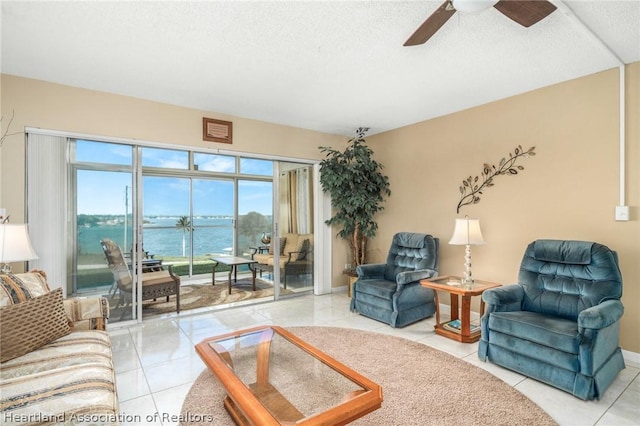 tiled living room featuring a textured ceiling, a water view, and ceiling fan