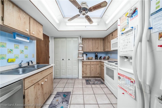 kitchen with white appliances, sink, ceiling fan, light tile patterned floors, and a tray ceiling