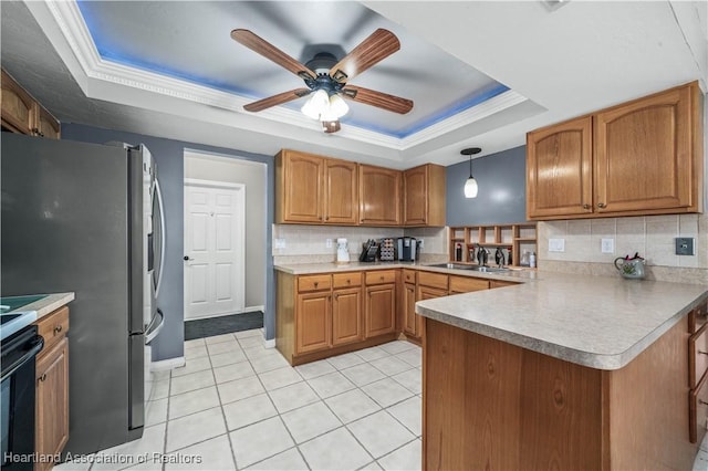 kitchen featuring sink, stainless steel refrigerator, a tray ceiling, kitchen peninsula, and pendant lighting