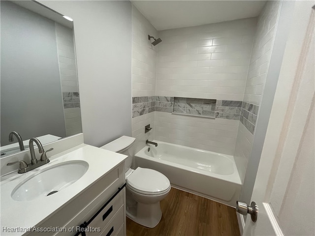 full bathroom with hardwood / wood-style floors, vanity, tiled shower / bath combo, and toilet