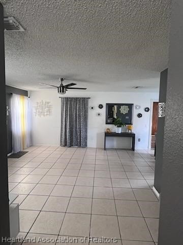 unfurnished living room featuring ceiling fan, light tile patterned flooring, and a textured ceiling