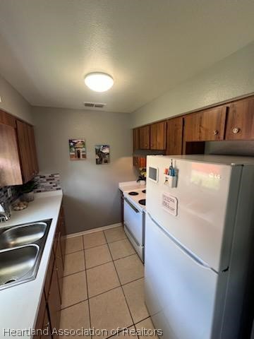 kitchen featuring light tile patterned floors, white appliances, and sink