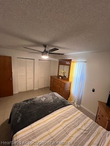 tiled bedroom with ceiling fan, a textured ceiling, and multiple closets