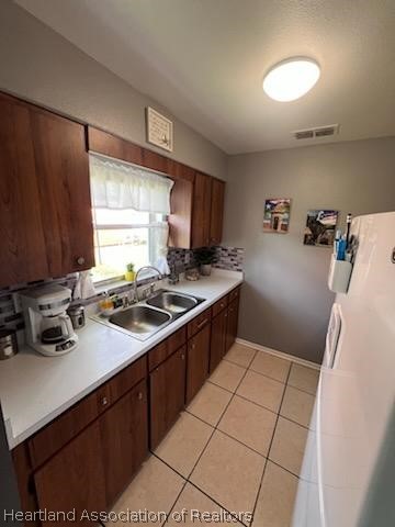 kitchen featuring dark brown cabinetry, light tile patterned floors, sink, and tasteful backsplash