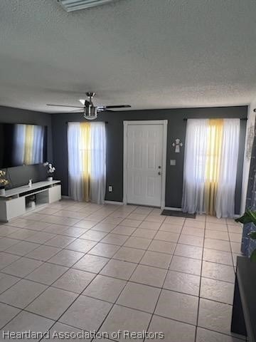 unfurnished living room with ceiling fan, plenty of natural light, light tile patterned floors, and a textured ceiling