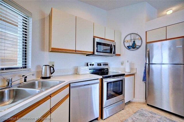 kitchen featuring light tile patterned floors, a sink, light countertops, white cabinets, and appliances with stainless steel finishes