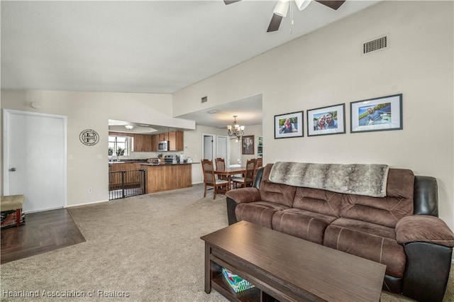 living room with ceiling fan with notable chandelier, carpet floors, and vaulted ceiling