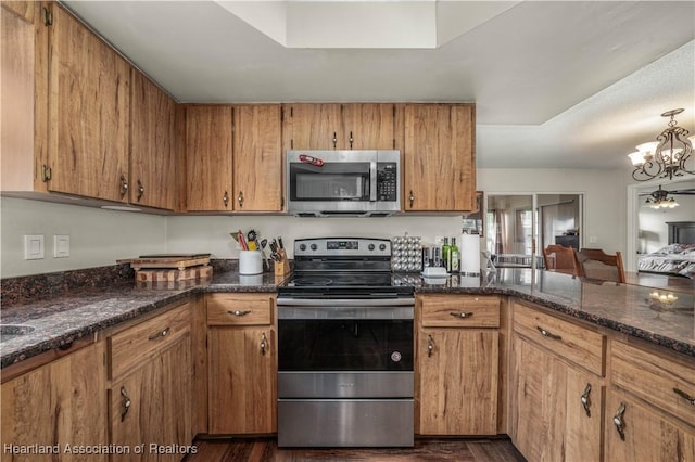 kitchen with appliances with stainless steel finishes, dark hardwood / wood-style floors, an inviting chandelier, and dark stone countertops