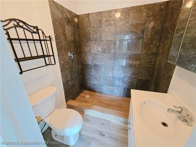 bathroom with toilet, vanity, wood-type flooring, and tiled shower