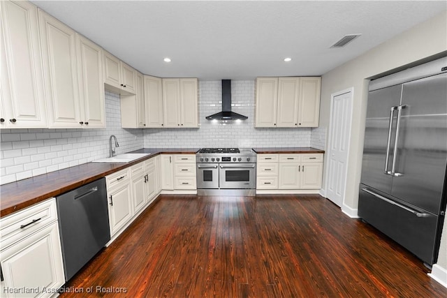 kitchen featuring high end appliances, backsplash, dark wood-type flooring, wall chimney range hood, and sink