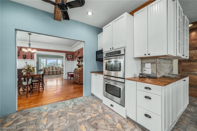 kitchen with ceiling fan with notable chandelier, butcher block counters, stainless steel double oven, and white cabinetry