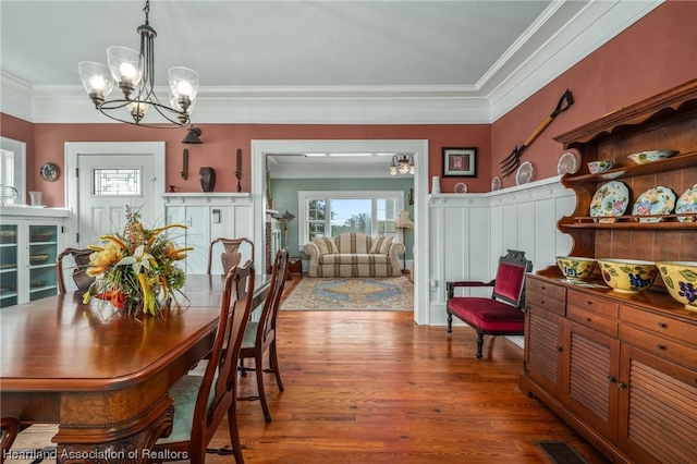 dining space featuring wood-type flooring, ornamental molding, and a notable chandelier