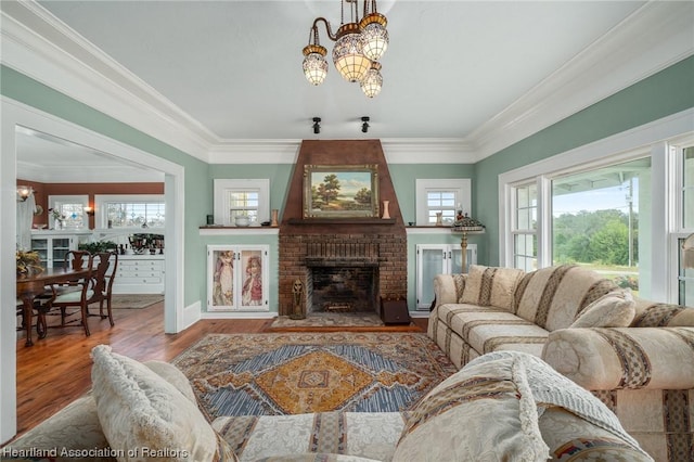 living room featuring hardwood / wood-style floors, an inviting chandelier, ornamental molding, and a brick fireplace