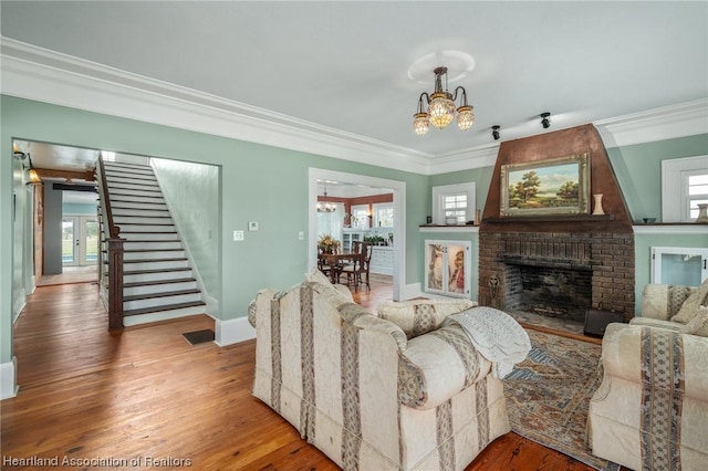 living room featuring hardwood / wood-style flooring, ornamental molding, a fireplace, and a chandelier