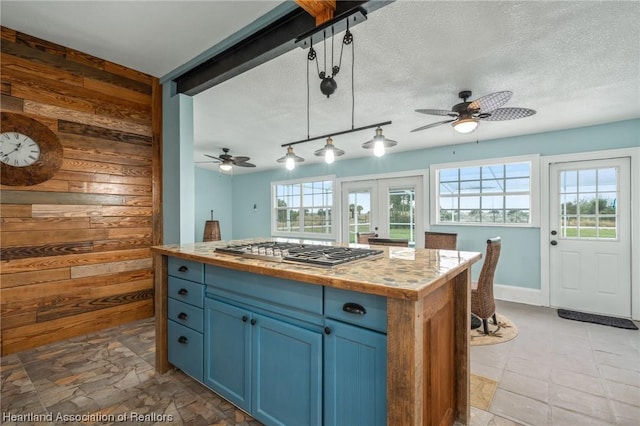 kitchen with blue cabinets, ceiling fan, wooden walls, decorative light fixtures, and stainless steel gas stovetop