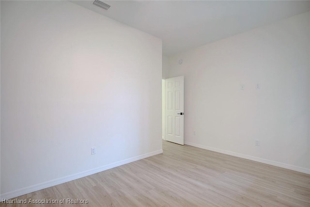 spare room with light wood-type flooring, visible vents, and baseboards