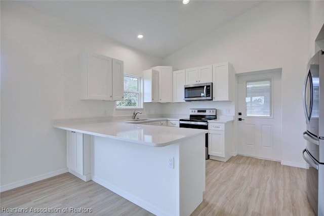 kitchen with a sink, stainless steel appliances, a peninsula, white cabinets, and light countertops