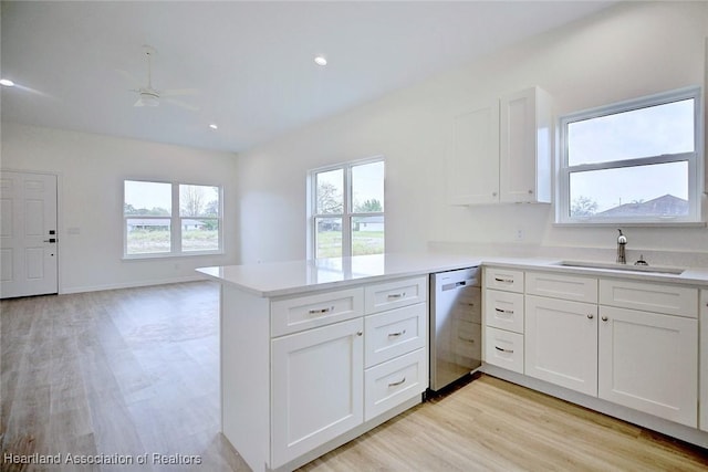 kitchen featuring dishwasher, light countertops, a peninsula, white cabinets, and a sink