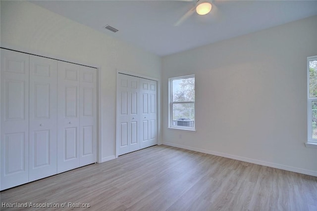 unfurnished bedroom with multiple windows, visible vents, multiple closets, and light wood finished floors