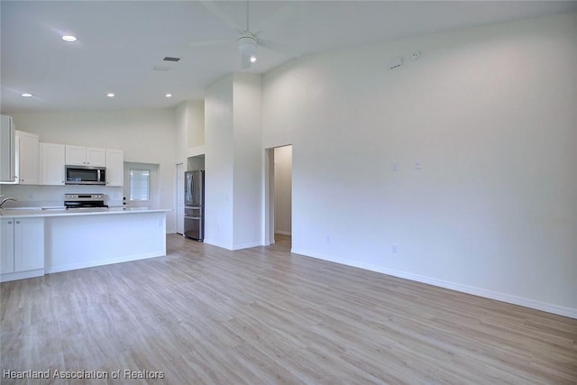 kitchen featuring light wood-type flooring, a ceiling fan, open floor plan, stainless steel appliances, and light countertops