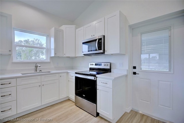 kitchen with a sink, white cabinetry, appliances with stainless steel finishes, light countertops, and lofted ceiling