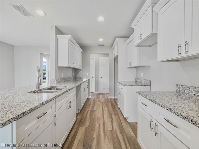 kitchen featuring sink, stainless steel dishwasher, light wood-type flooring, light stone counters, and white cabinetry