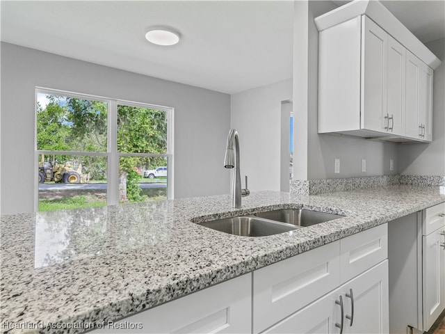 kitchen with light stone counters, white cabinetry, and sink