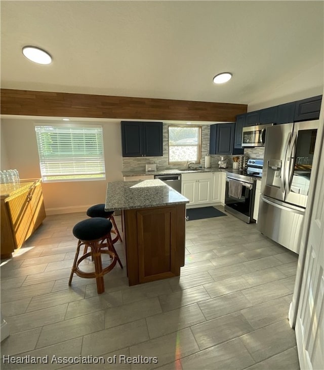 kitchen with backsplash, a kitchen breakfast bar, appliances with stainless steel finishes, a kitchen island, and light stone counters