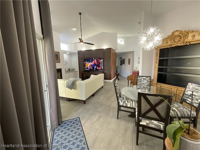 dining room featuring high vaulted ceiling, ceiling fan with notable chandelier, and light wood-type flooring