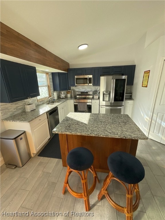 kitchen featuring white cabinetry, light stone countertops, a kitchen breakfast bar, decorative backsplash, and appliances with stainless steel finishes