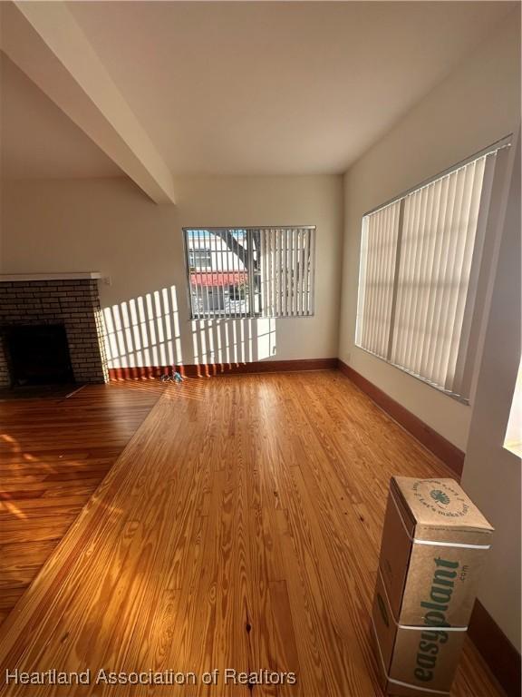 unfurnished living room featuring hardwood / wood-style flooring, beam ceiling, and a brick fireplace