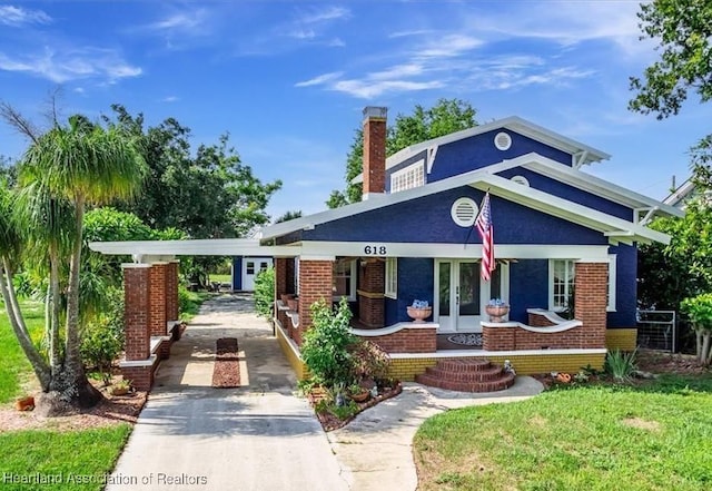 view of front of home with a carport, covered porch, a front yard, and french doors