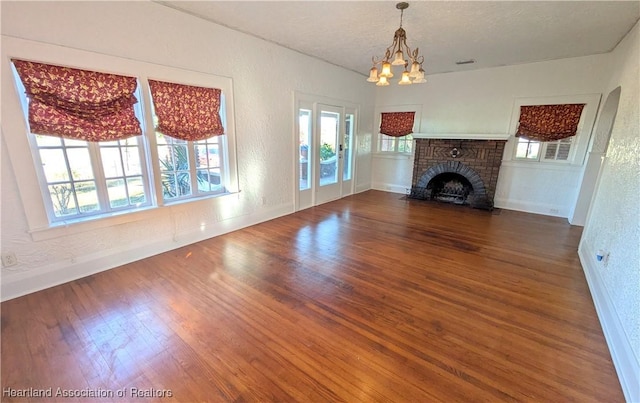 unfurnished living room featuring wood-type flooring, an inviting chandelier, a brick fireplace, and a healthy amount of sunlight