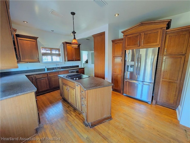 kitchen featuring sink, hanging light fixtures, stainless steel appliances, a kitchen island, and light wood-type flooring