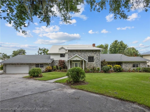 view of front of property with an attached garage, stone siding, a chimney, aphalt driveway, and a front lawn