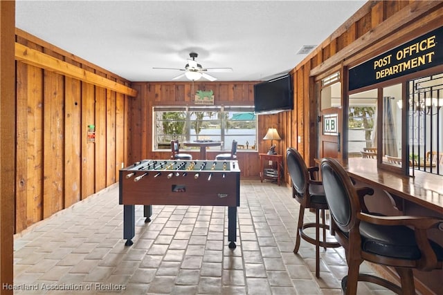 game room with wood walls, ceiling fan, and visible vents