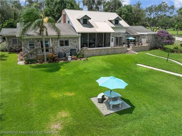 back of property with stone siding, a sunroom, a lawn, and central air condition unit