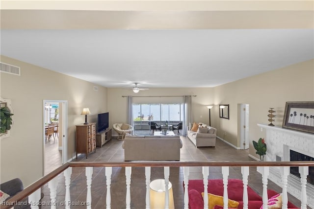 tiled living room with a fireplace, visible vents, baseboards, and ceiling fan