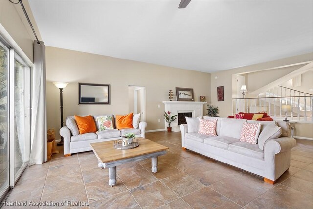 living room featuring baseboards, a fireplace with raised hearth, and stairs