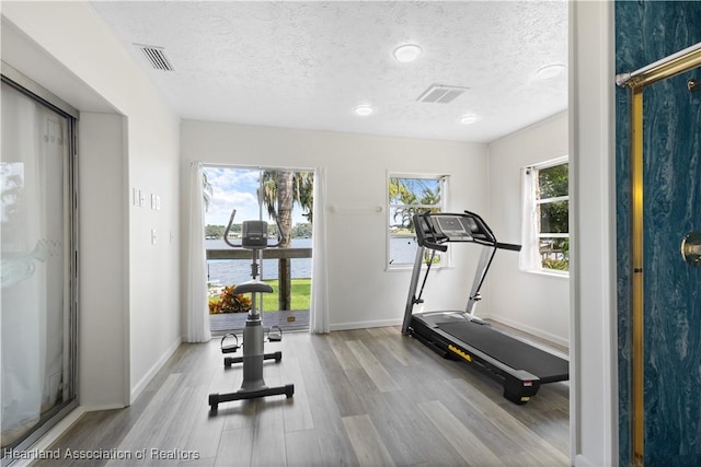 exercise area featuring visible vents, baseboards, a textured ceiling, and wood finished floors