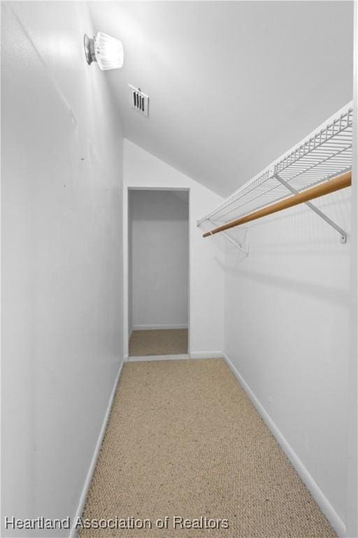 walk in closet featuring visible vents, light colored carpet, and lofted ceiling