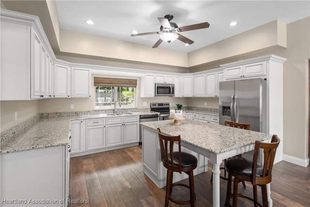 kitchen featuring a ceiling fan, a kitchen island, a breakfast bar area, appliances with stainless steel finishes, and a sink