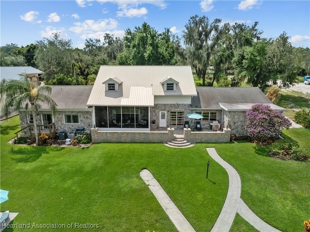 rear view of property with stone siding, metal roof, a lawn, and a patio