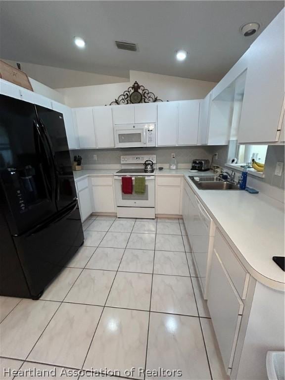 kitchen with white appliances, sink, vaulted ceiling, light tile patterned flooring, and white cabinetry