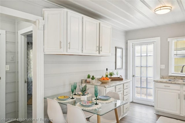 kitchen with sink, light stone countertops, ornamental molding, light hardwood / wood-style floors, and white cabinetry